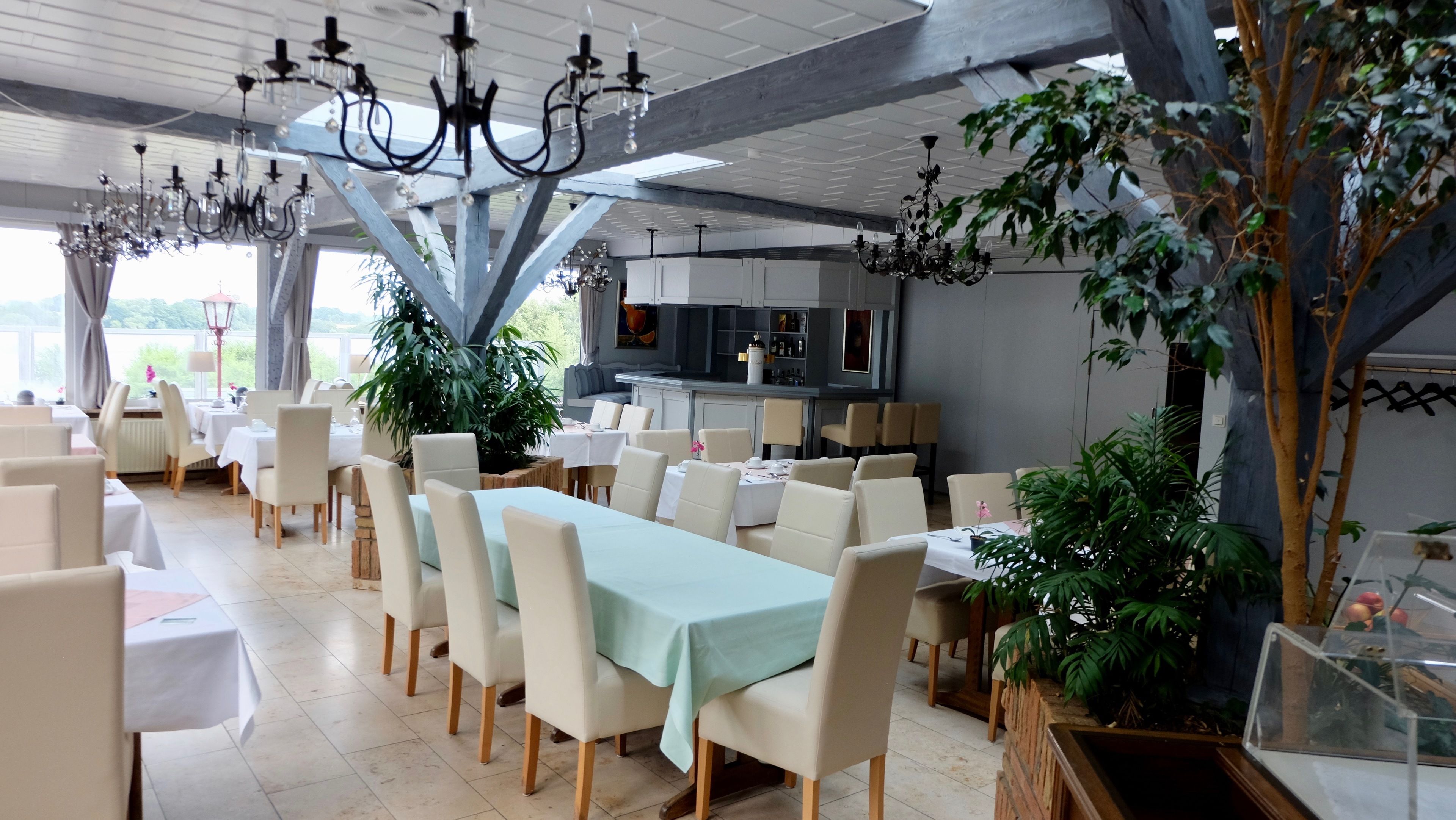 A spacious dining area with multiple tables and chairs, a bar area, and several potted plants.