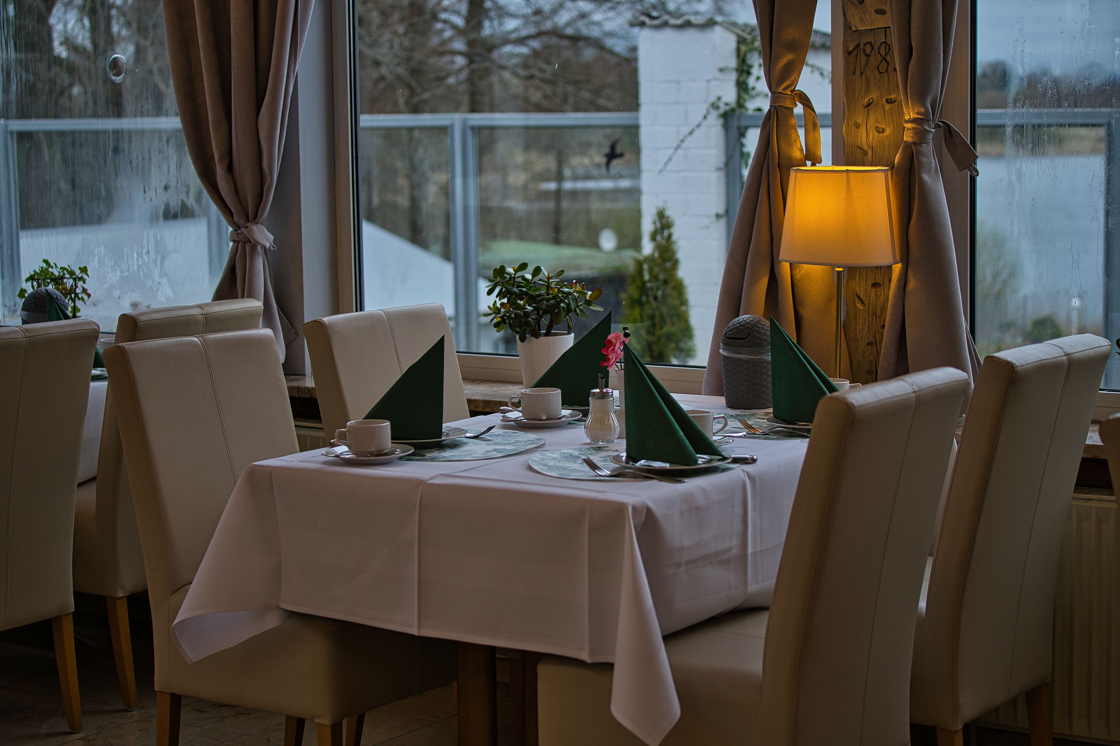 A dining table set for four with a white tablecloth, chairs, and a lamp.