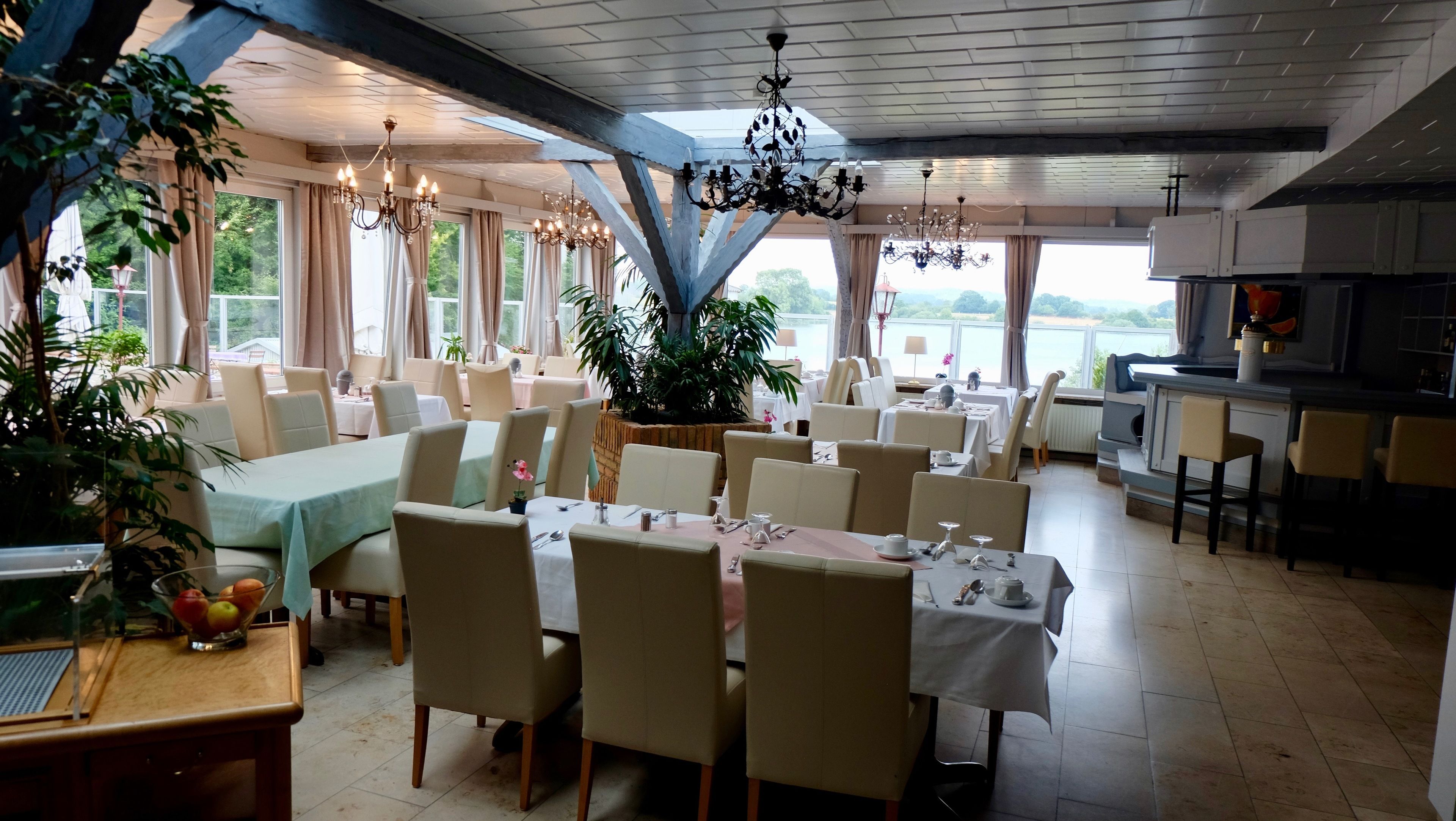 Un restaurante con varias mesas y sillas, ventanas amplias y vistas al exterior.