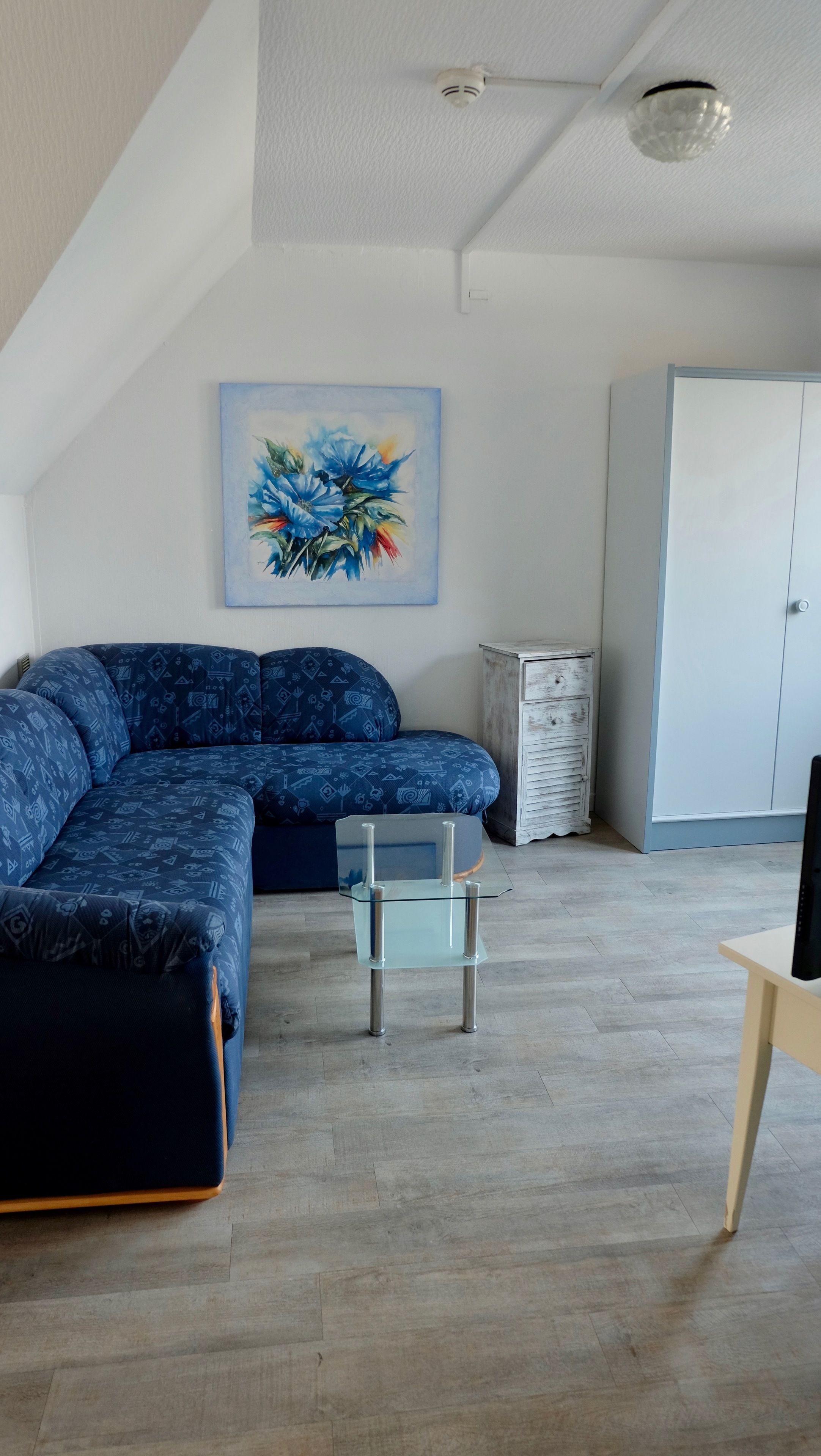 Una sala de estar moderna con un sofá modular, una mesa de centro de vidrio, un armario blanco y un cuadro en la pared.