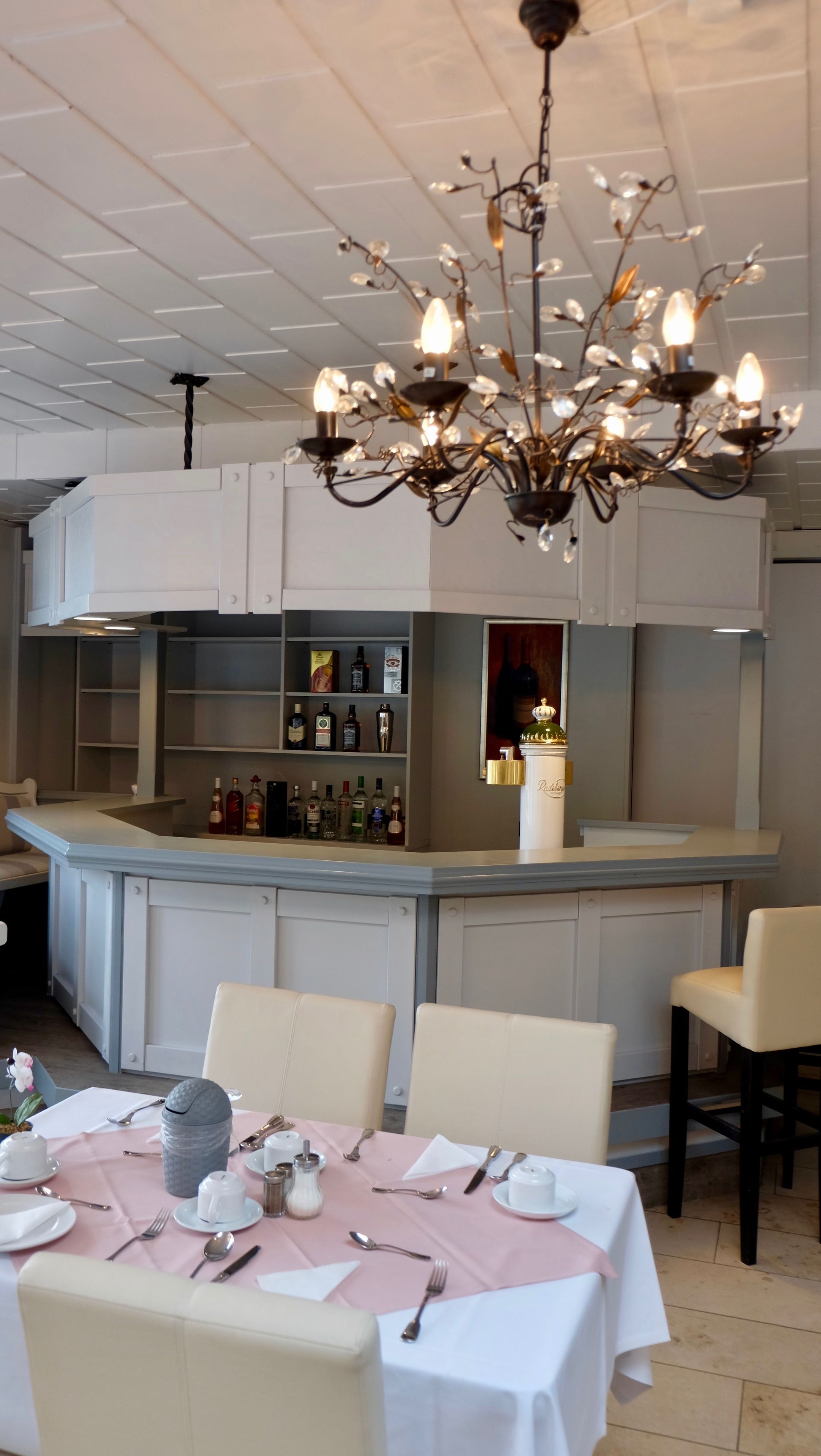 Interior de restaurante con barra, mesas dispuestas con vajilla blanca y un candelabro.