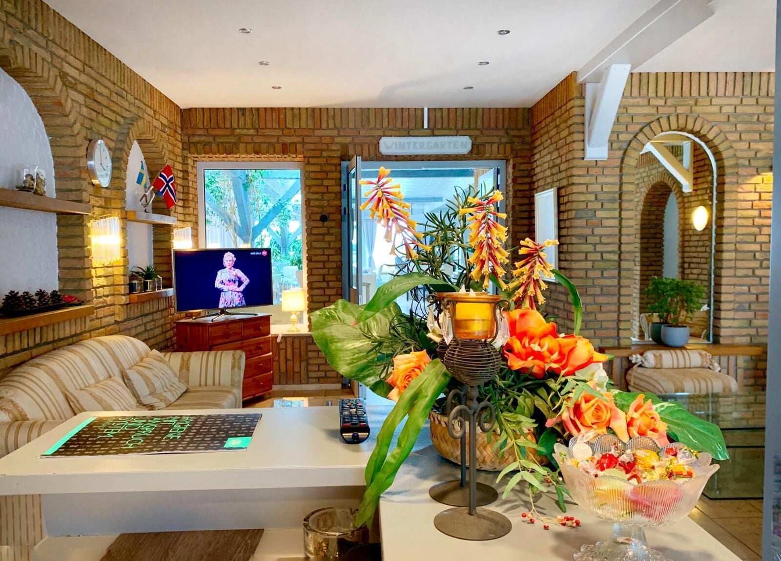 A modern living room with a brick wall, a television, a sofa, a coffee table, and a decorative plant arrangement.