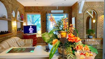 A modern living room with a brick wall, a television, a sofa, a coffee table, and a decorative plant arrangement.
