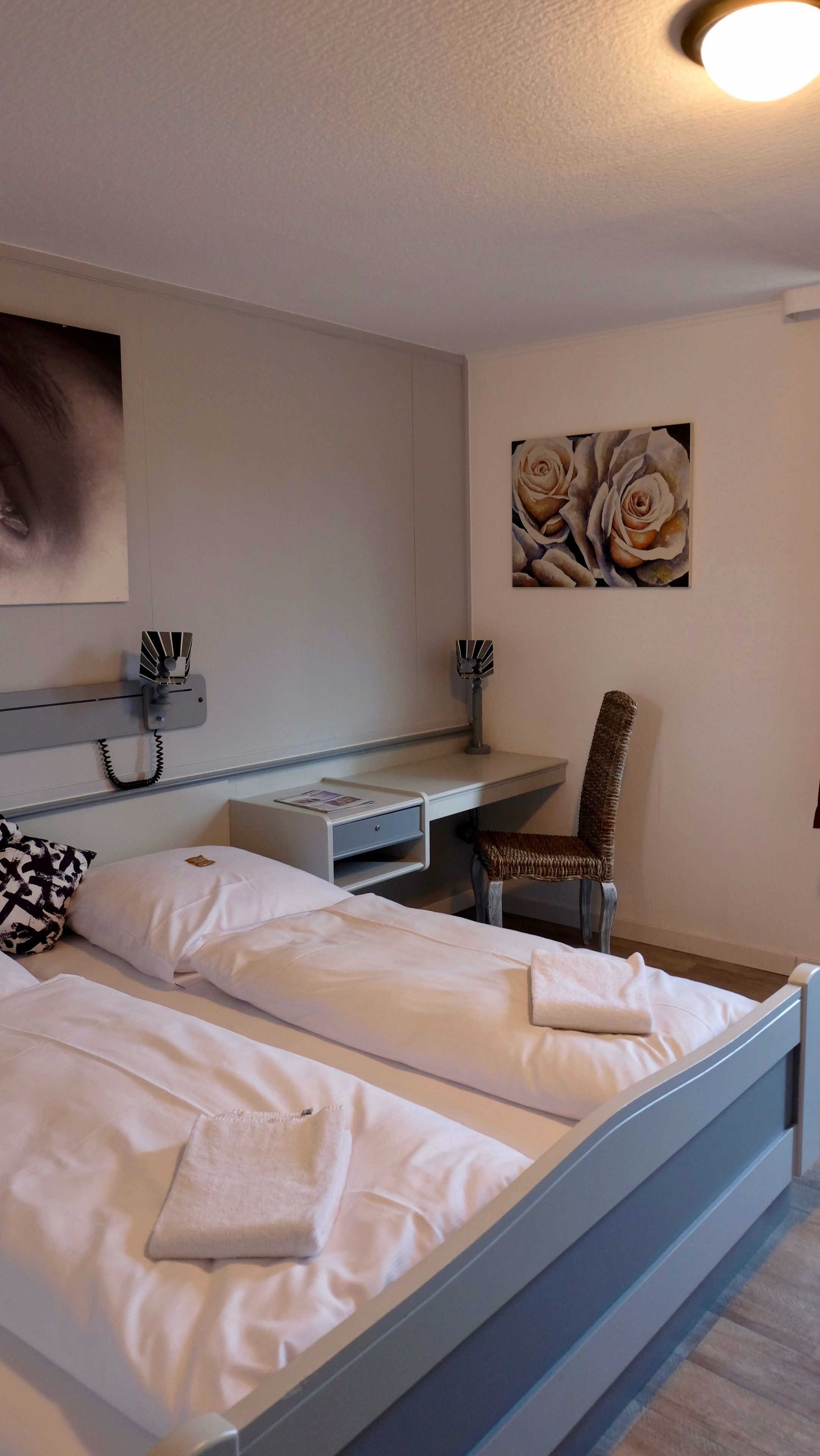 A hotel room with a bed, a desk, a chair, and a painting on the wall.