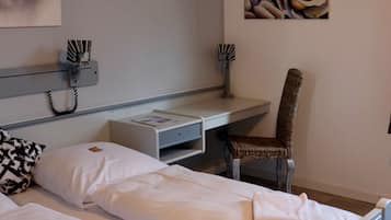A hotel room with a bed, a desk, a chair, and a painting on the wall.