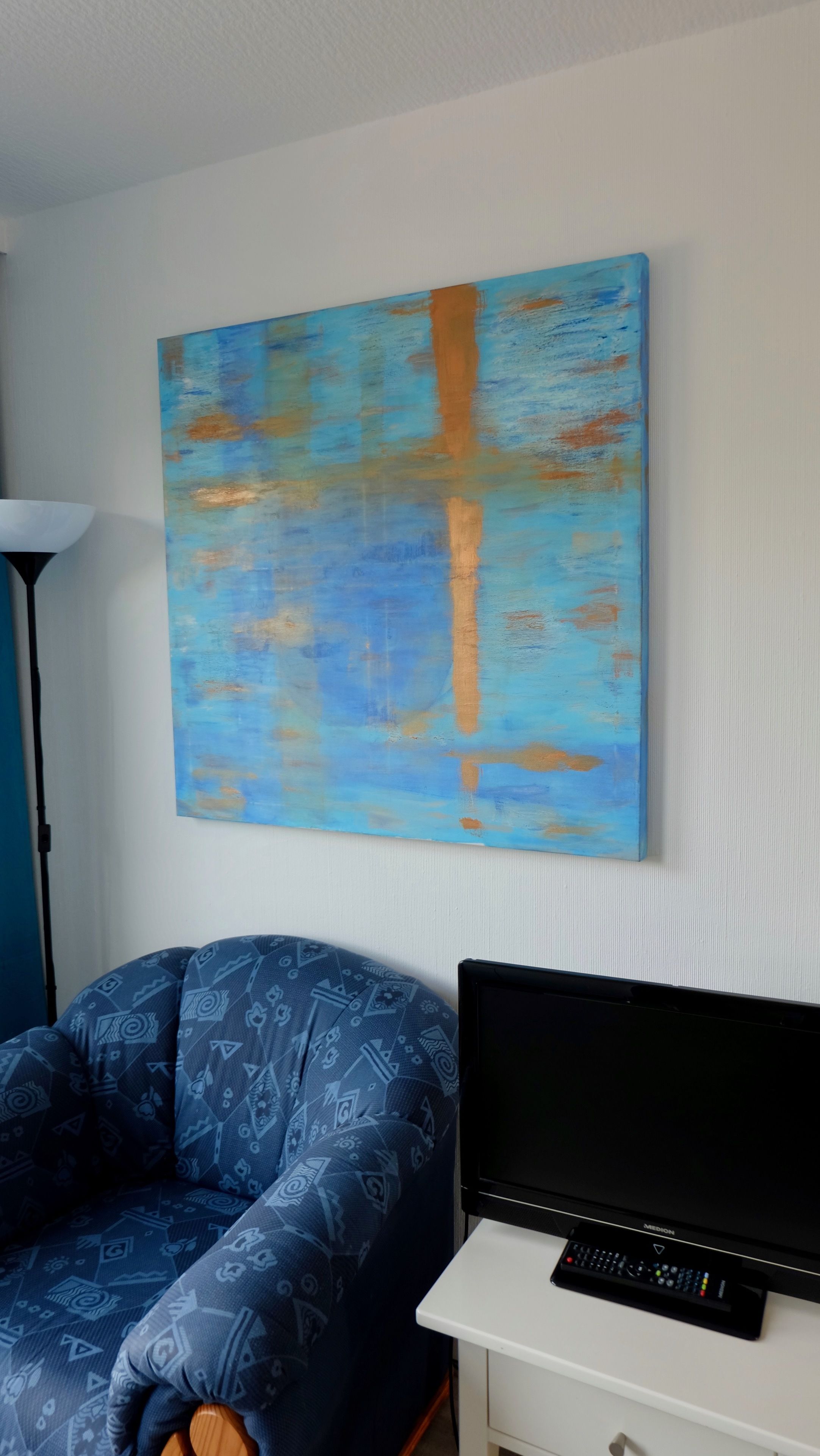 A room with a blue patterned sofa, a flat-screen TV on a white stand, and a large abstract painting on the wall.