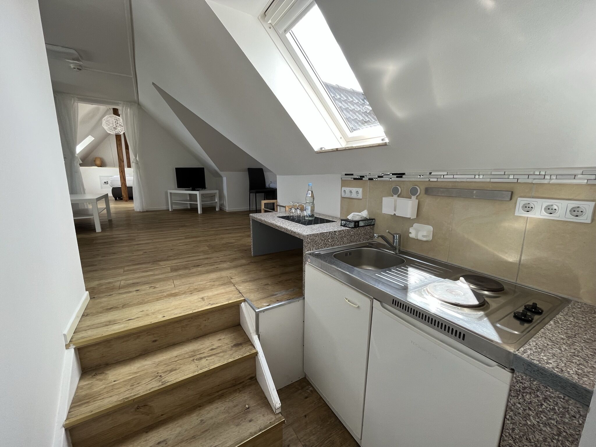 Una cocina moderna con tragaluz, escalera de madera y zona de comedor con mesa y sillas.
