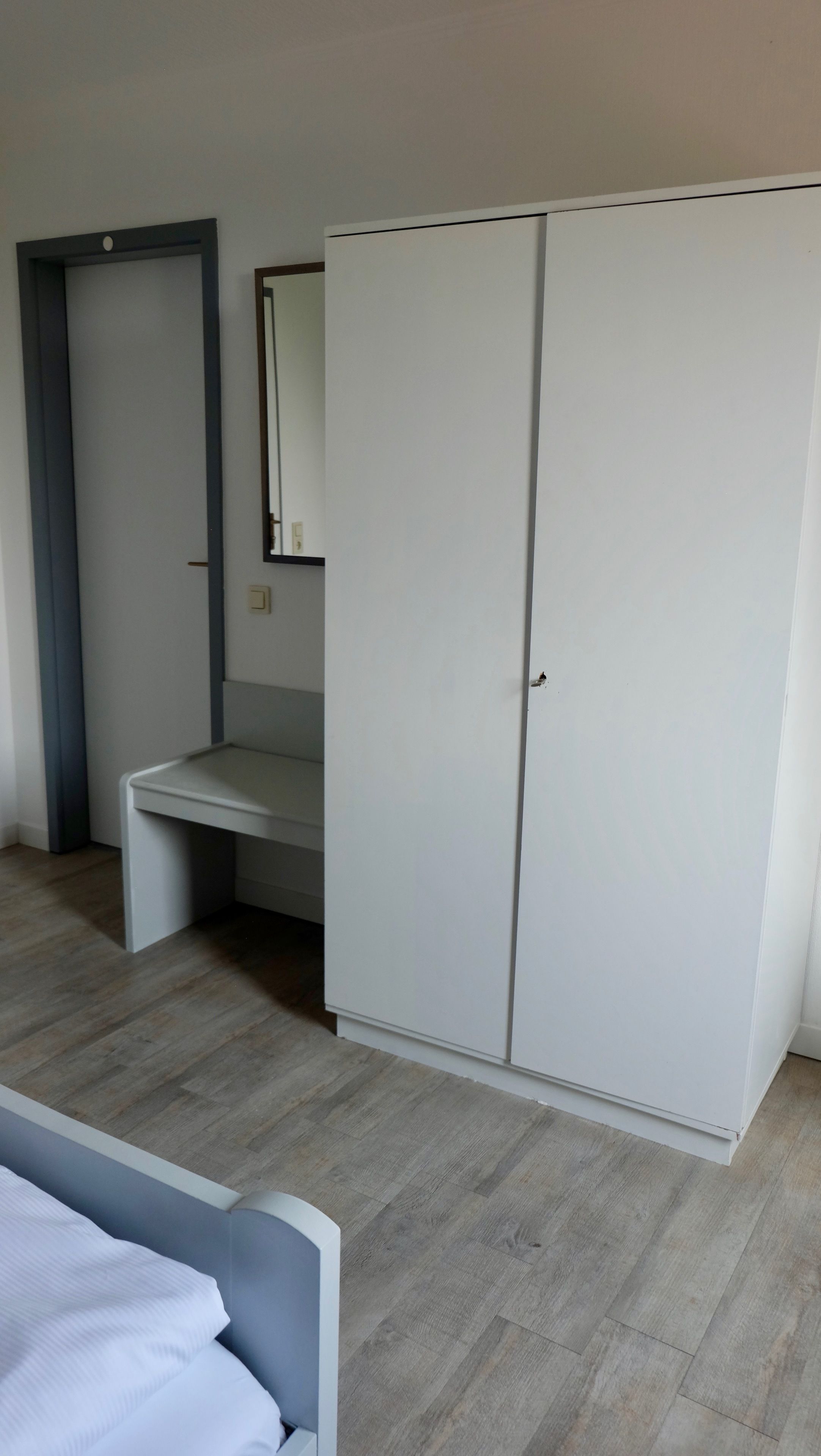 Une chambre à coucher avec un lit, une armoire, un miroir et un petit bureau.