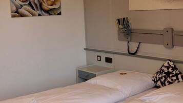 A bedroom with two beds, a painting of roses, a large eye artwork, and a bedside table with a lamp.