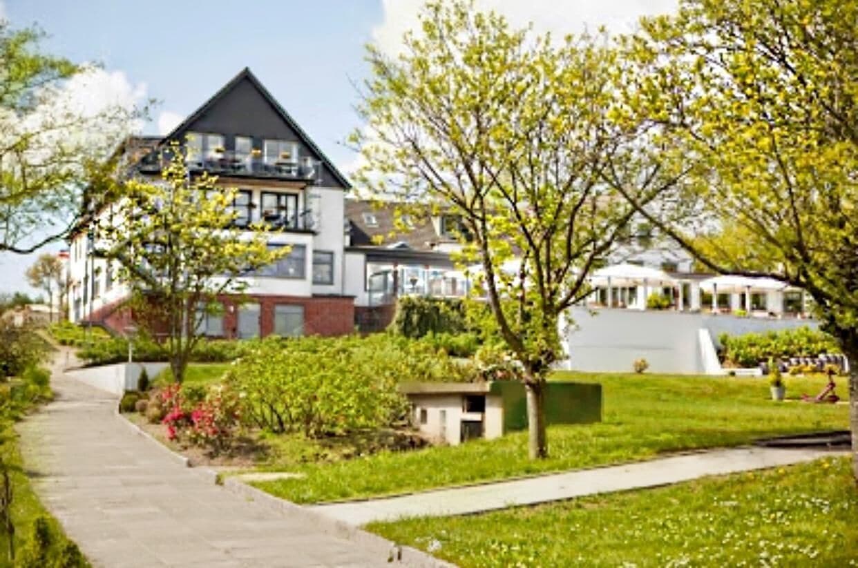 Um edifício residencial moderno com telhado inclinado, várias varandas e um jardim bem cuidado com um caminho.