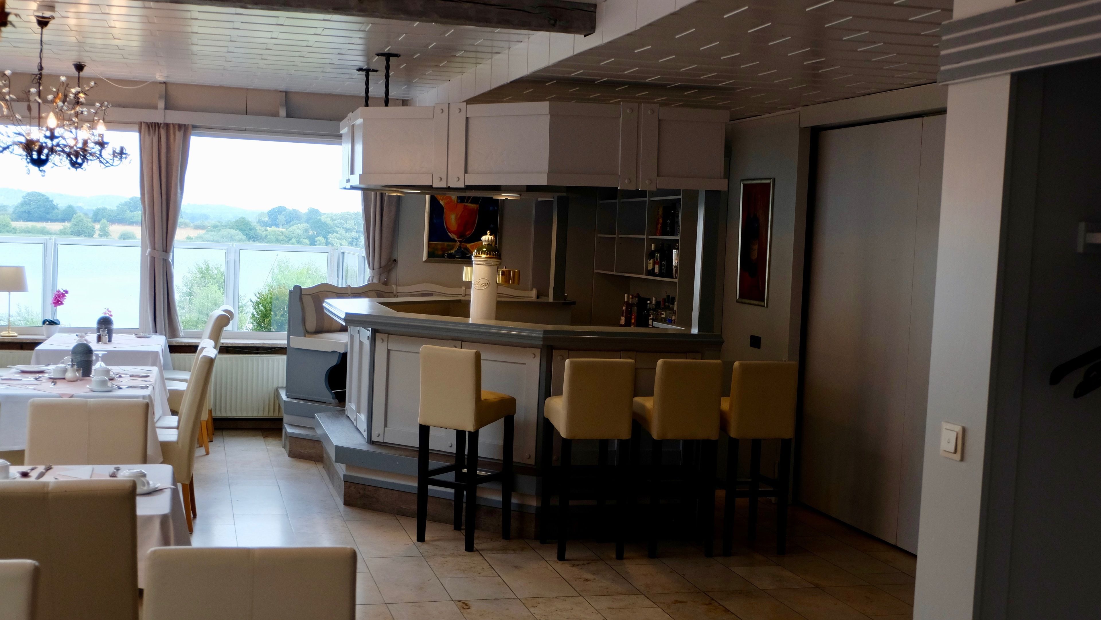 A modern kitchen with a bar area, dining space, and large windows offering a view of the outdoors.