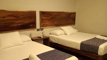 A hotel room with two beds, wooden headboards, white linens, and a small bedside table with a bottle and remote control.