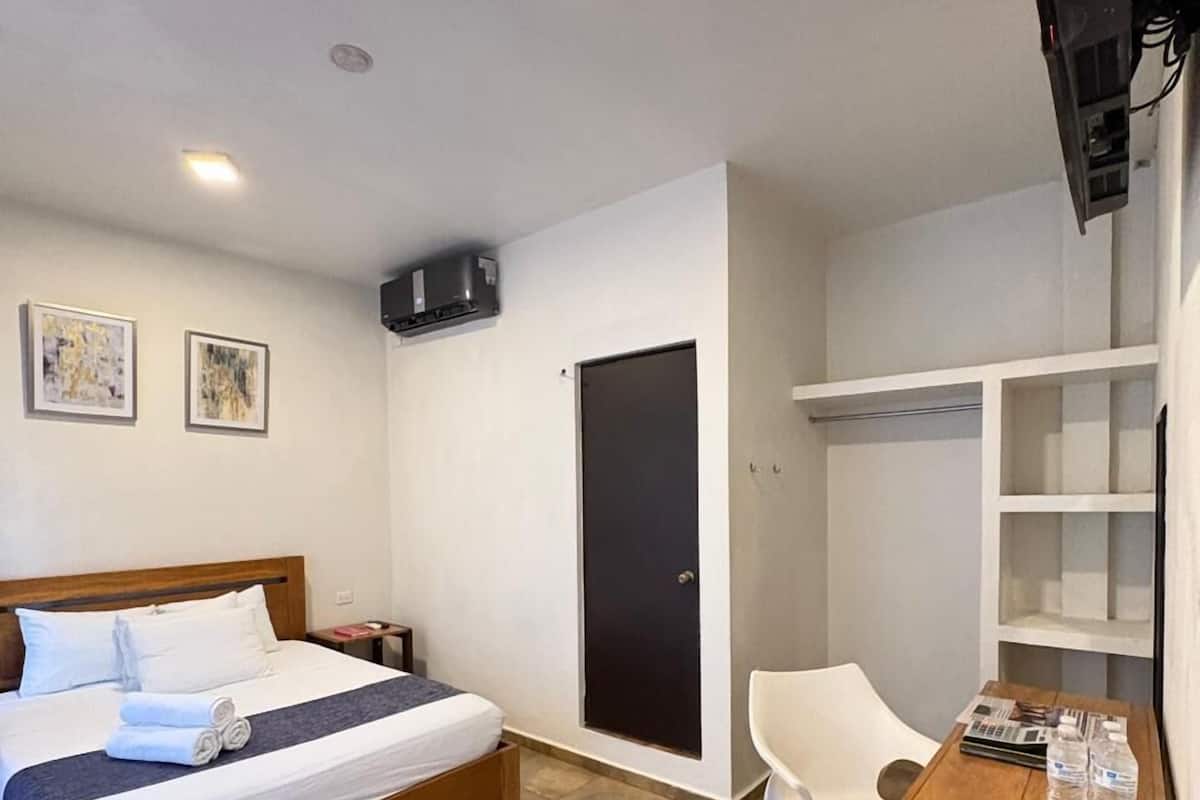 Habitación de hotel con cama, escritorio, silla, armario y televisor.