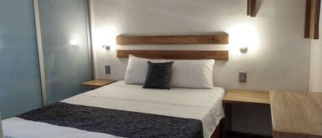 Un dormitorio con cama, mesitas de noche, cabecera de madera y lámpara fijada a la pared.