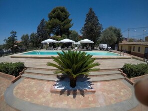 A swimming pool with lounge chairs and umbrellas, surrounded by trees and a paved area. - B&B il giardino di Agata (Mascalucia)
