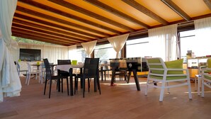 An open-plan living area with a dining table and chairs, a grill, and large windows with curtains. - B&B il giardino di Agata (Mascalucia)