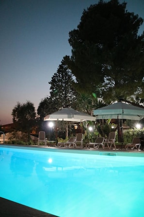 A swimming pool with lounge chairs and umbrellas, surrounded by trees and buildings. - B&B il giardino di Agata (Mascalucia)