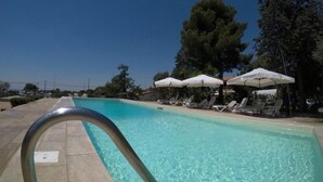 A swimming pool with clear water, surrounded by lounge chairs and umbrellas. - B&B il giardino di Agata (Mascalucia)