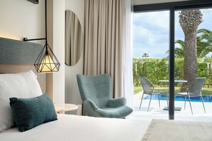 Un dormitorio moderno con una cama grande, un sillón verde azulado y vistas a una piscina y palmeras.