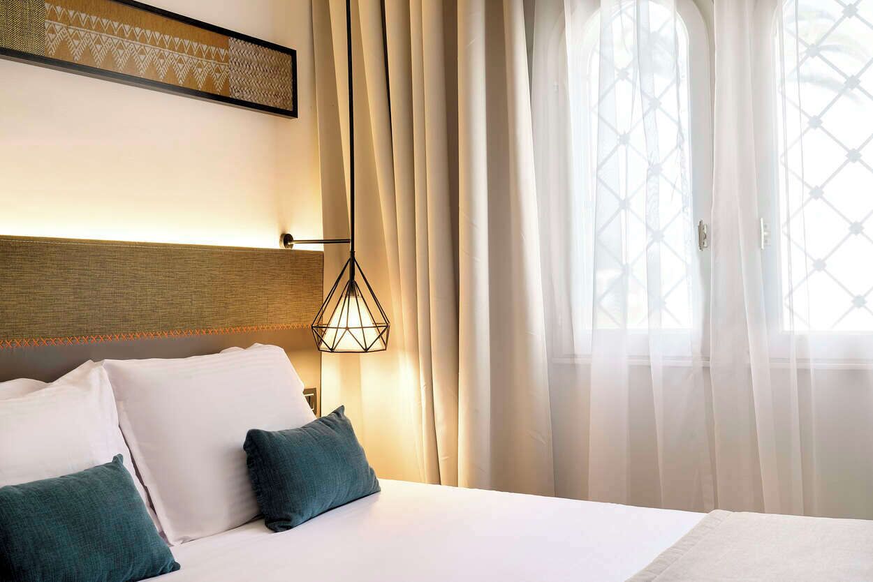 Een hotelkamer met een bed, een wandlamp en dunne gordijnen.