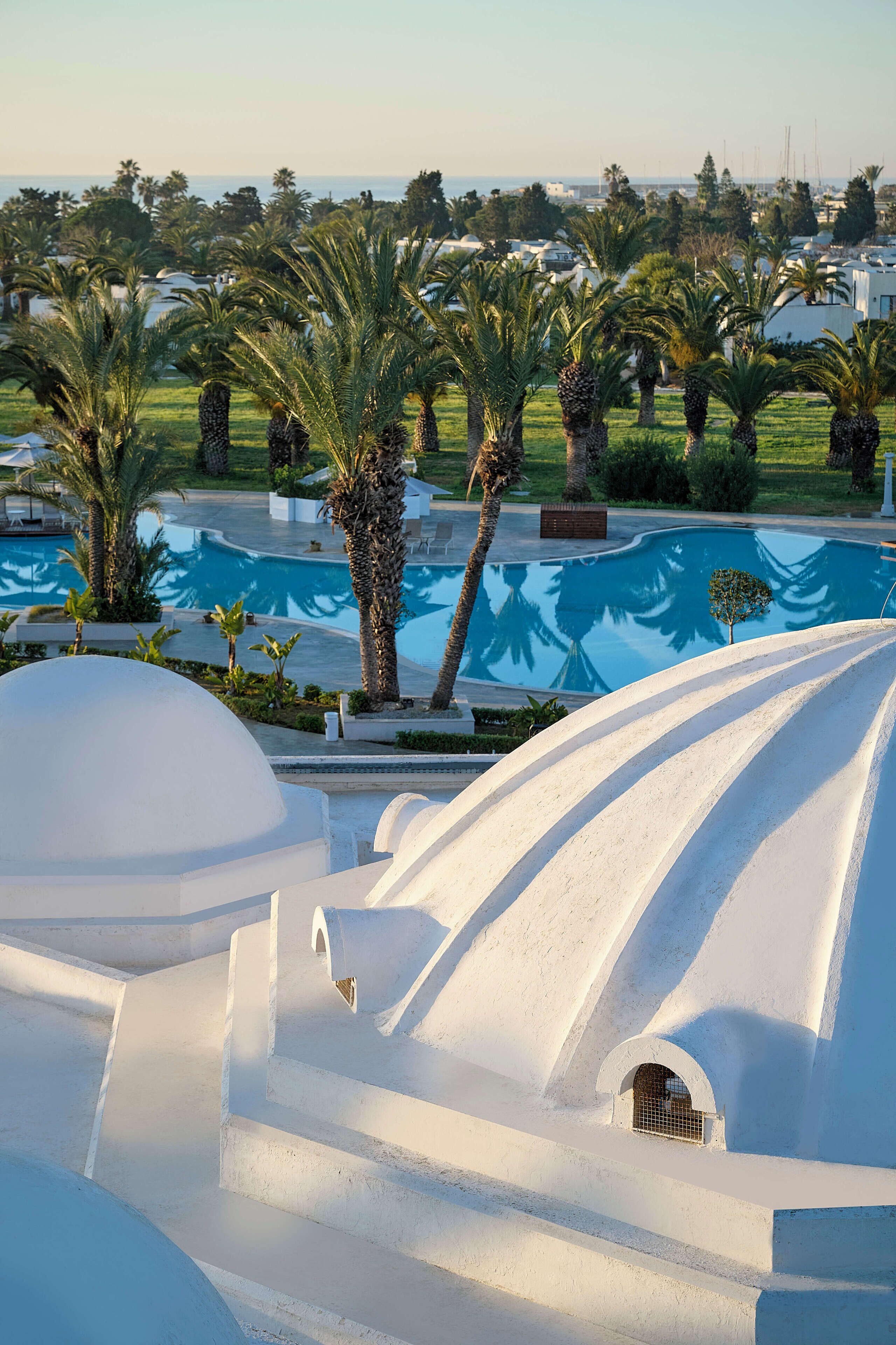 A resort with white domed structures, a swimming pool, and palm trees.