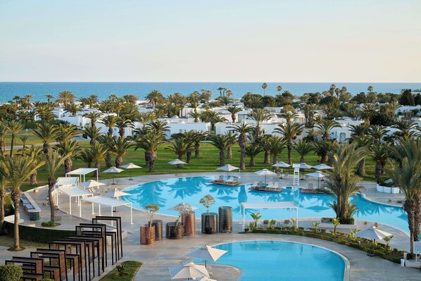 A resort with a large pool, palm trees, and a view of the sea. - The Mirage Resort & SPA (Hammamet)