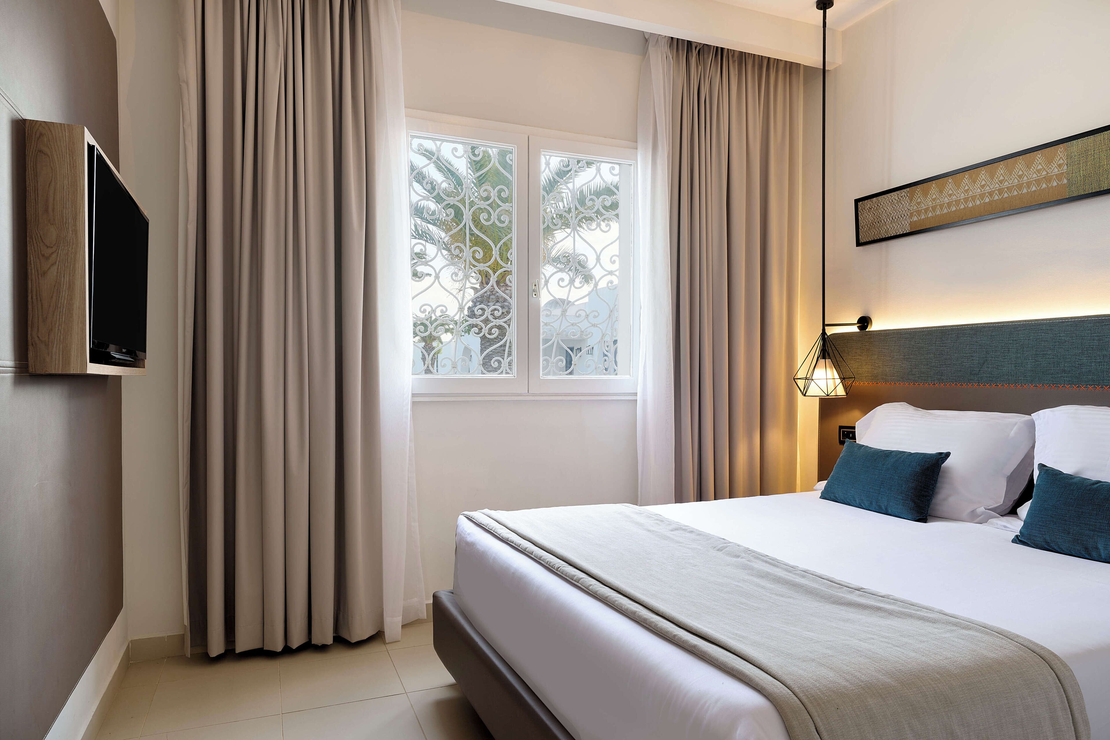 A hotel room with a bed, curtains, a TV, and a window with a view.