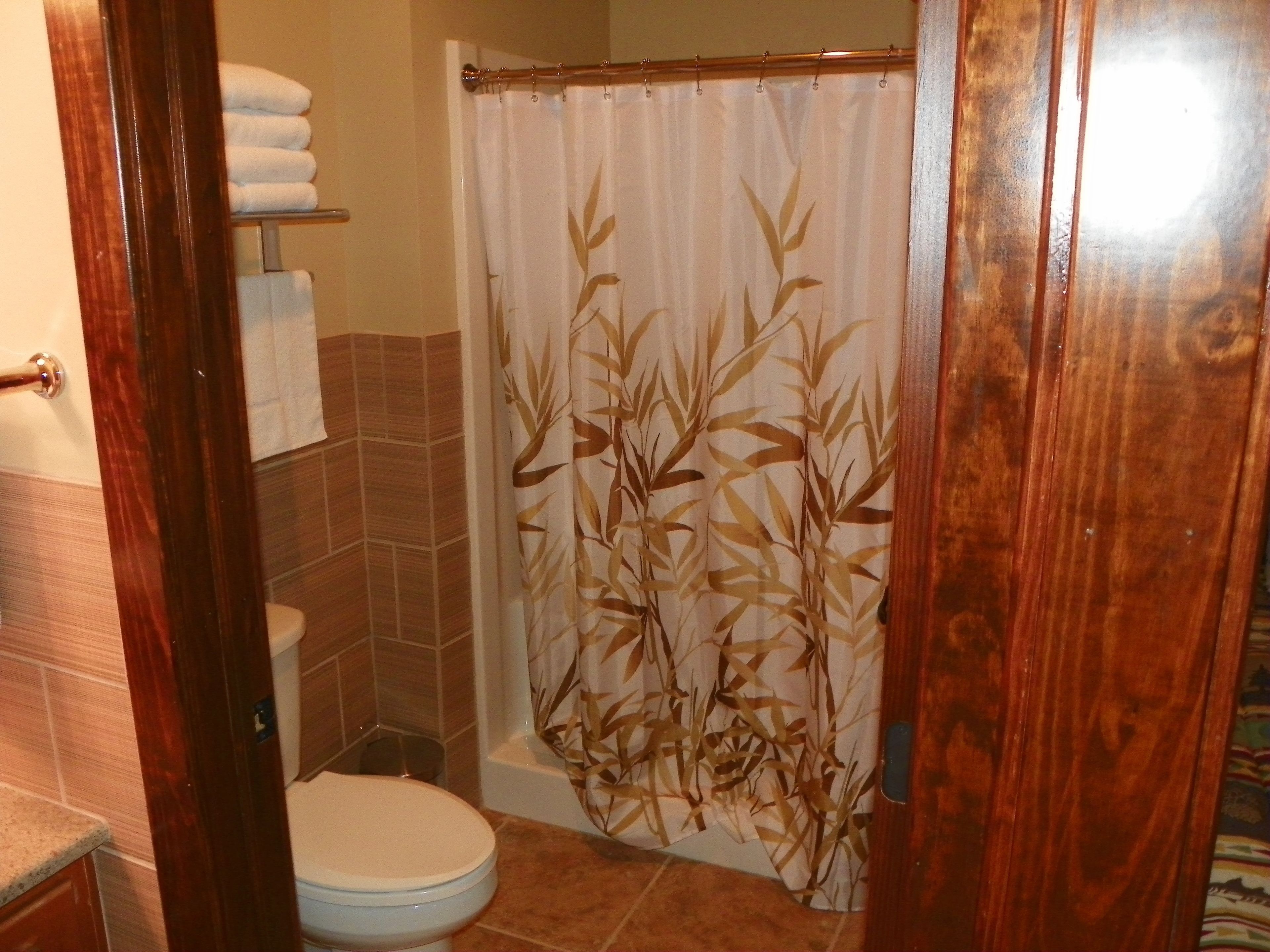 A bathroom with a toilet, a shower curtain with a bamboo pattern, and a towel rack with folded towels.