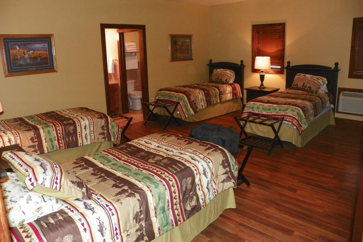 A room with two beds, a wooden floor, a painting on the wall, and a door leading to a bathroom.