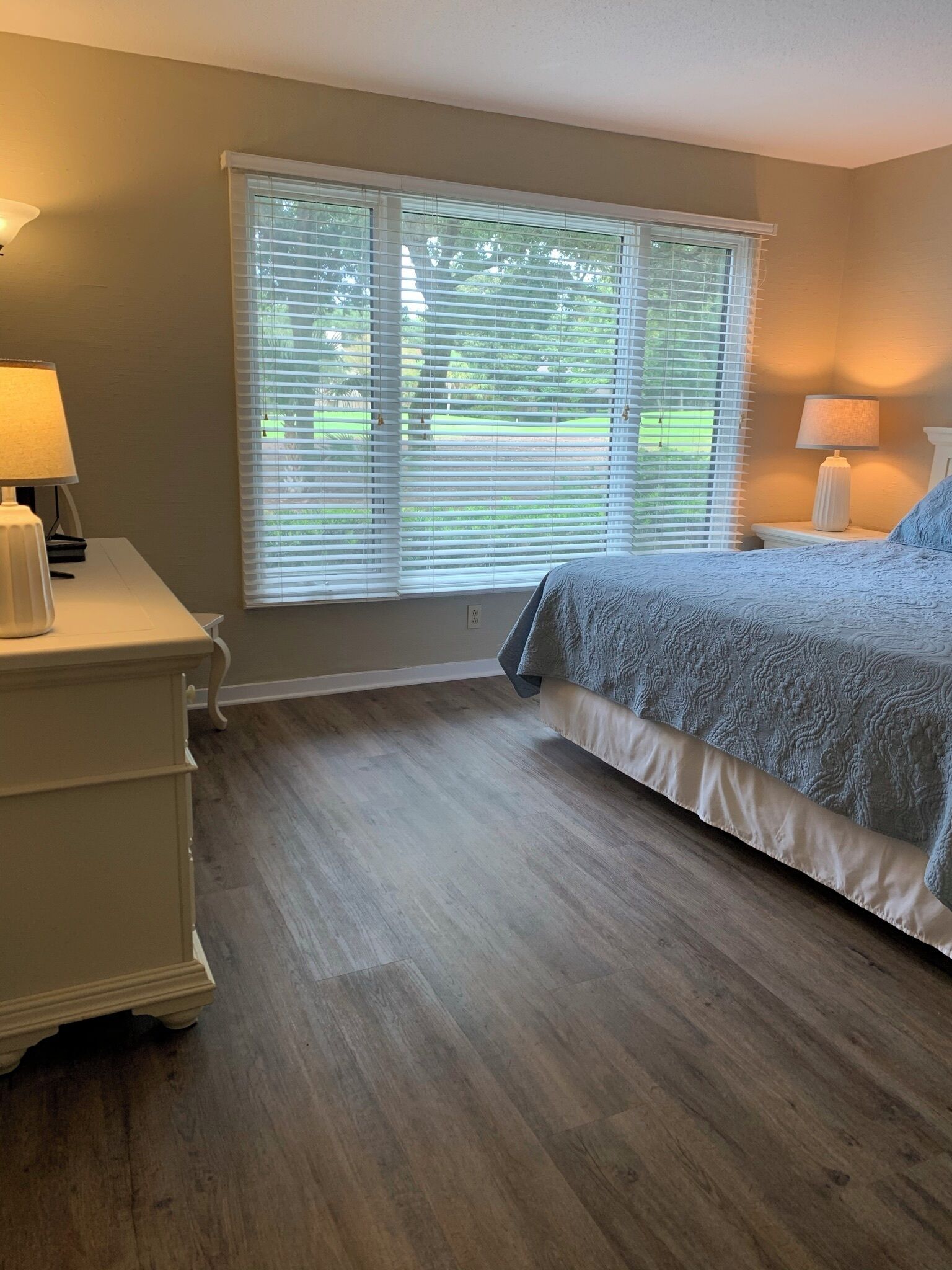 A bedroom with a bed, two bedside tables, a window with blinds, and a lamp on each table.