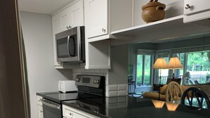 A modern kitchen with white cabinets, a black countertop, stainless steel appliances, and a view of the outdoors.