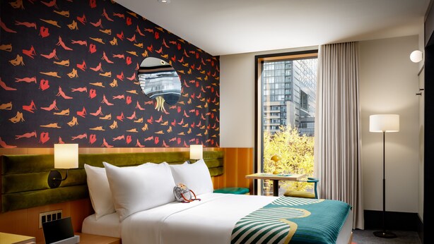 Une chambre d’hôtel avec un grand lit, une table de chevet, un bureau et une vue sur la ville grâce à une grande fenêtre.