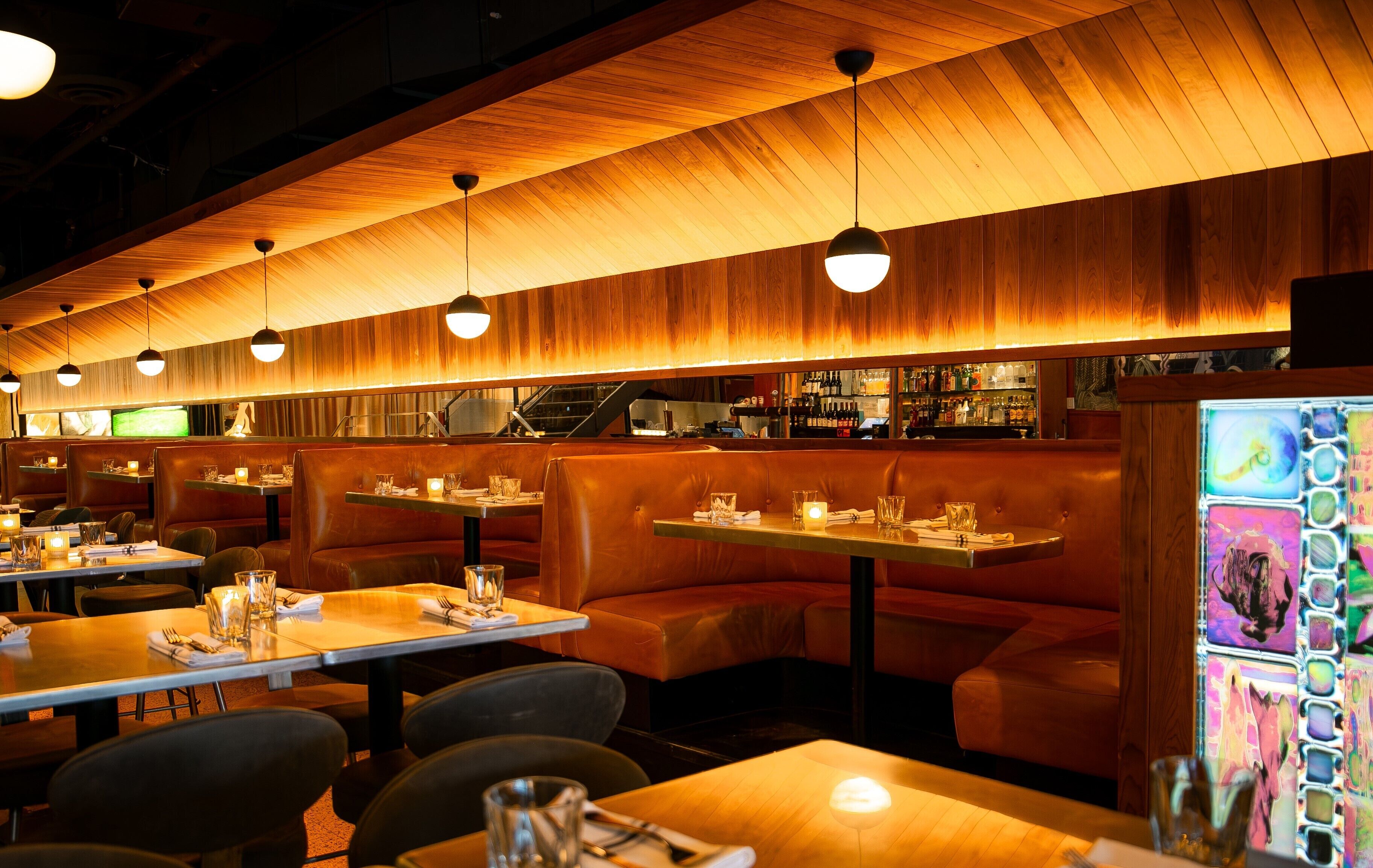 Un restaurant avec des murs lambrissés, des banquettes en cuir et des luminaires suspendus. Les tables sont dressées avec des verres et des couverts.