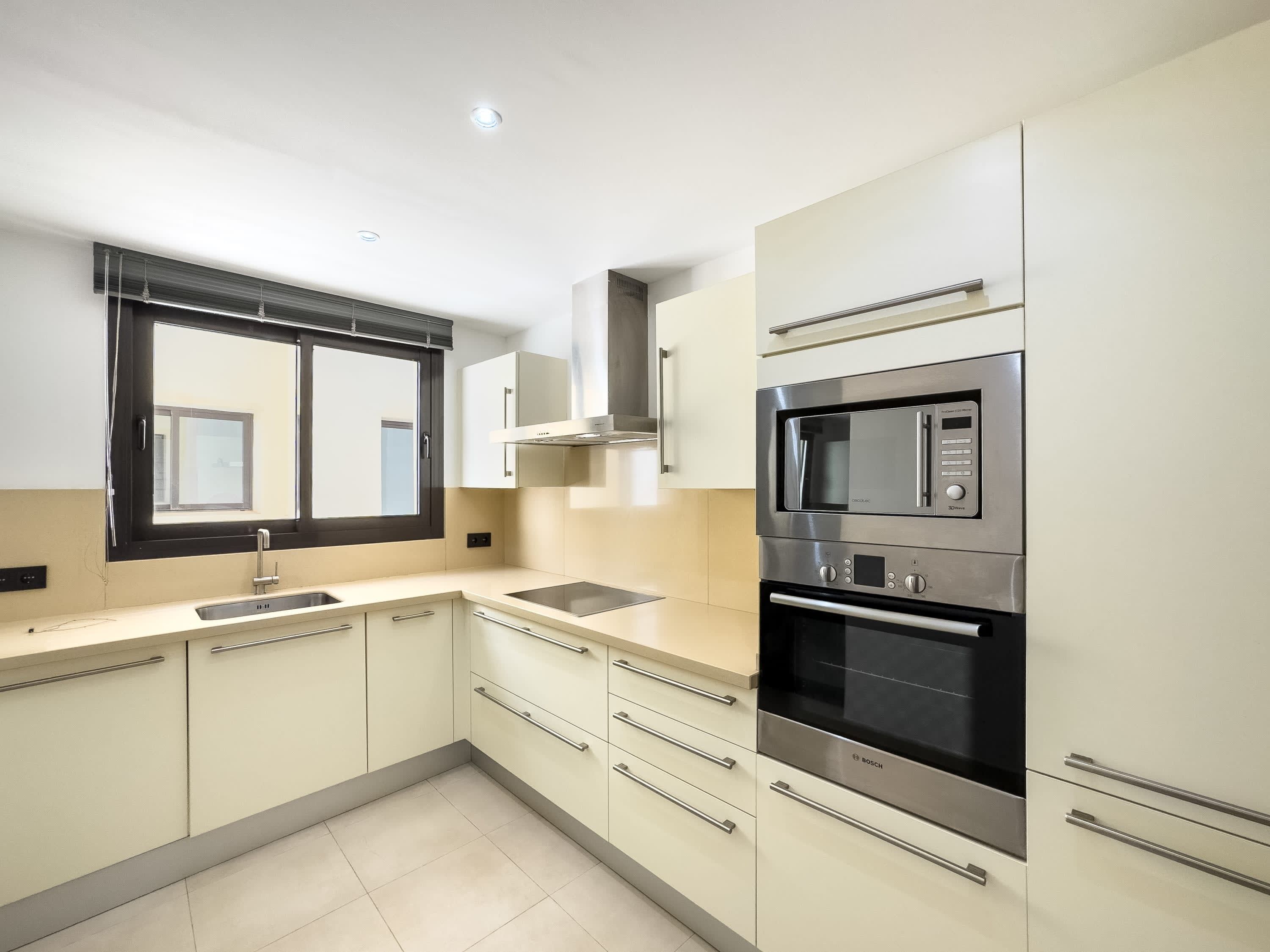 A modern kitchen with a Bosch oven, a microwave, a sink, and a window with blinds.