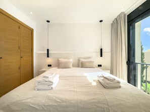 A modern bedroom with a large bed, two bedside tables, a wardrobe, and a balcony view.
