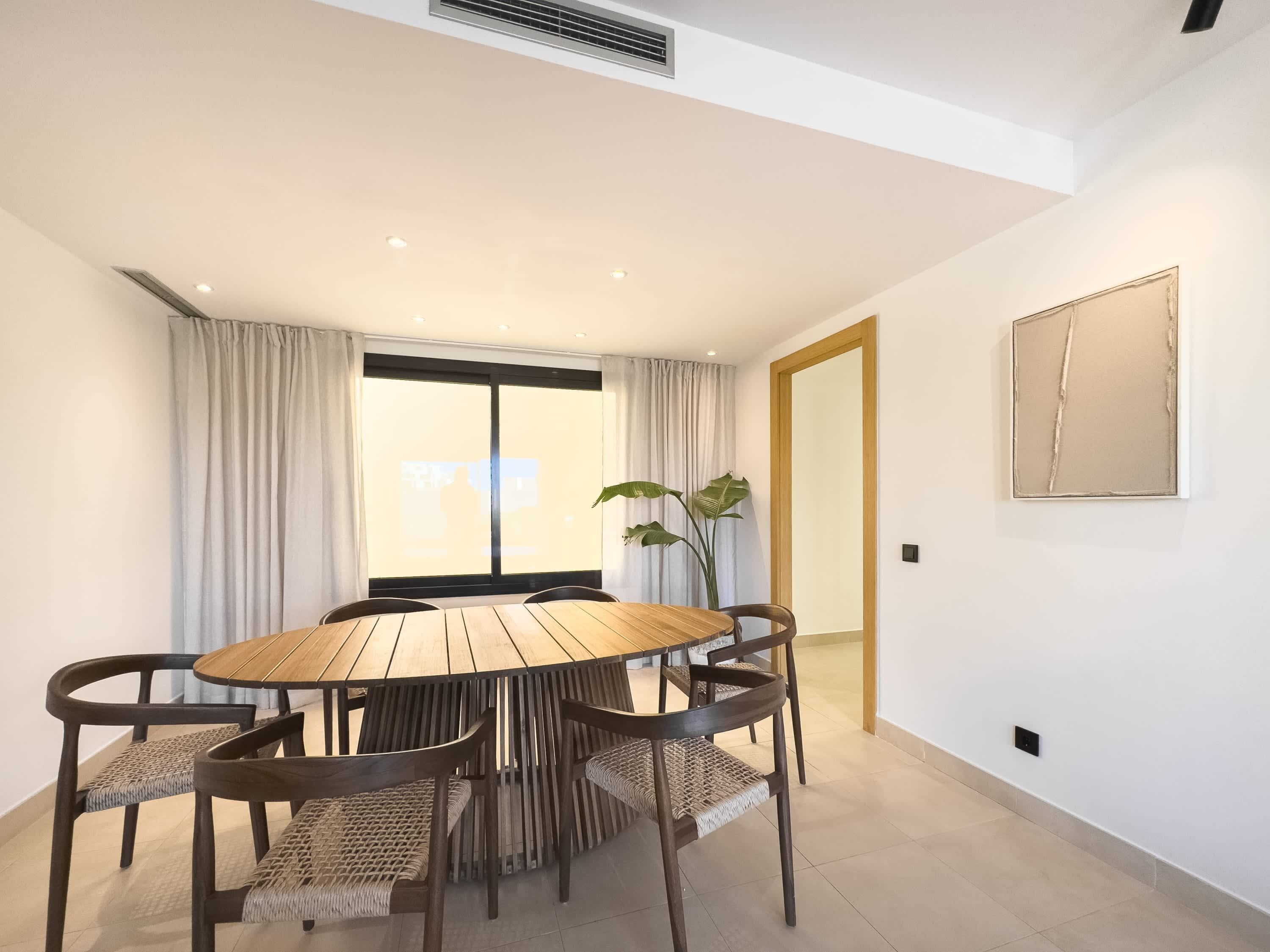 A modern dining area with a round table, dark chairs, and a large window with curtains.