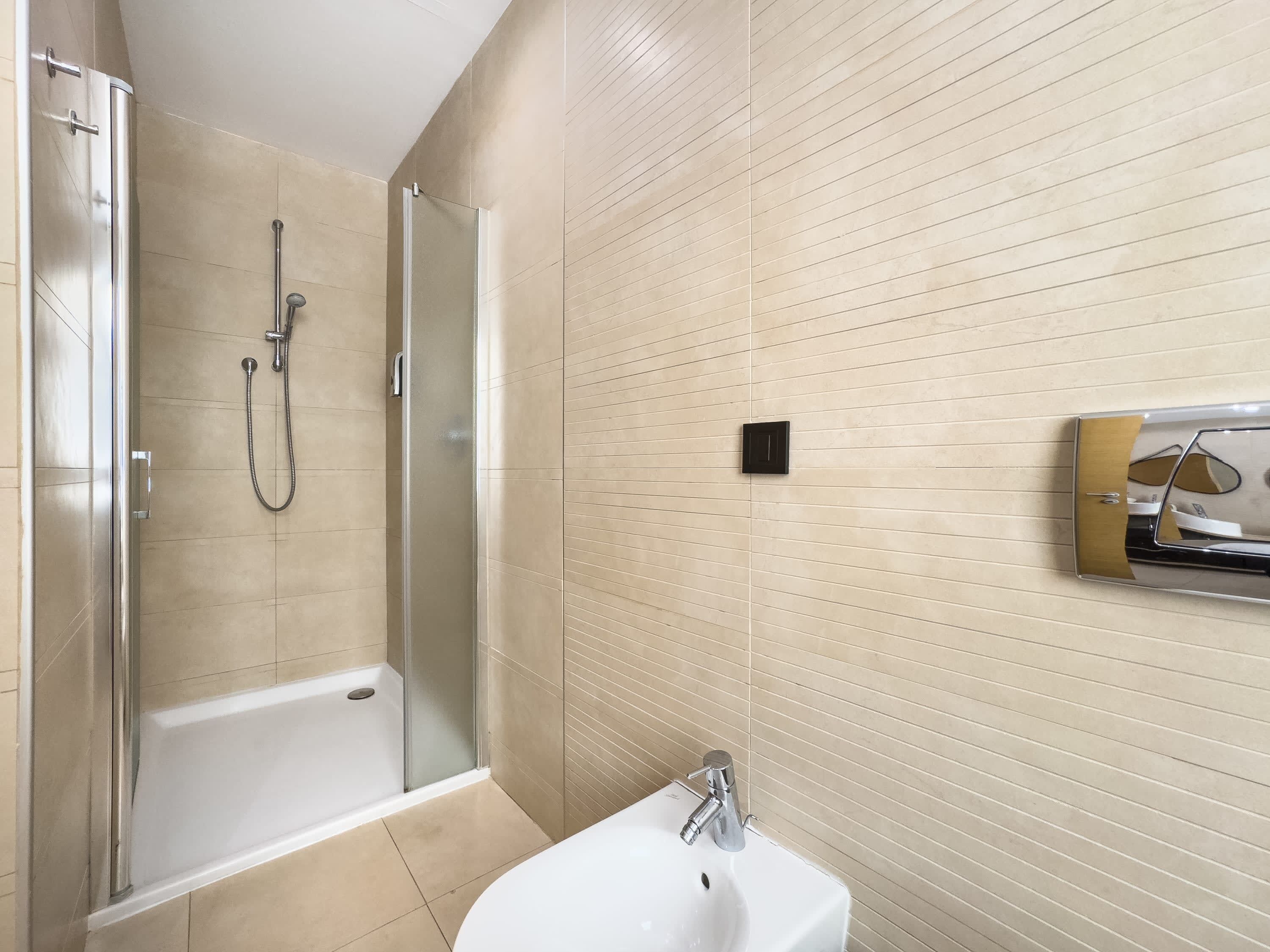 Un baño con ducha envuelta en cristal, un lavamanos blanco y un espejo con marco decorativo.