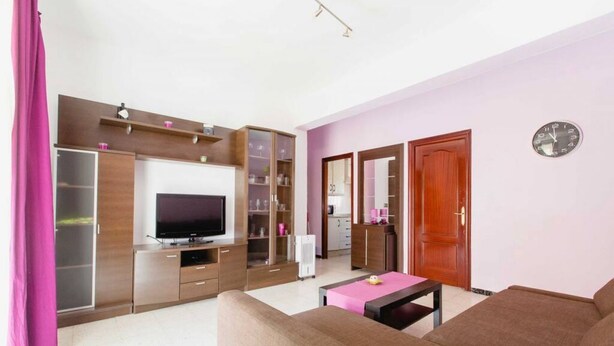 A modern living room with a flat-screen TV, built-in shelving, a sofa, and a coffee table. - Apartamento La dama de Cádiz (Cádiz)