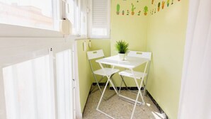 A small, bright room with a white door, a window with blinds, a white table with two chairs, and a wall decorated with potted plants. - Apartamento La dama de Cádiz (Cádiz)