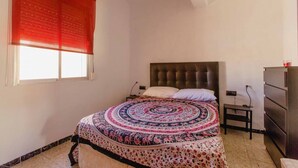 A bedroom with a bed, a headboard, a nightstand, a dresser, and a window with blinds. - Apartamento La dama de Cádiz (Cádiz)