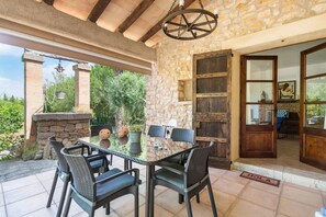 Un patio con una mesa y sillas de vidrio, paredes de piedra y una puerta de madera.