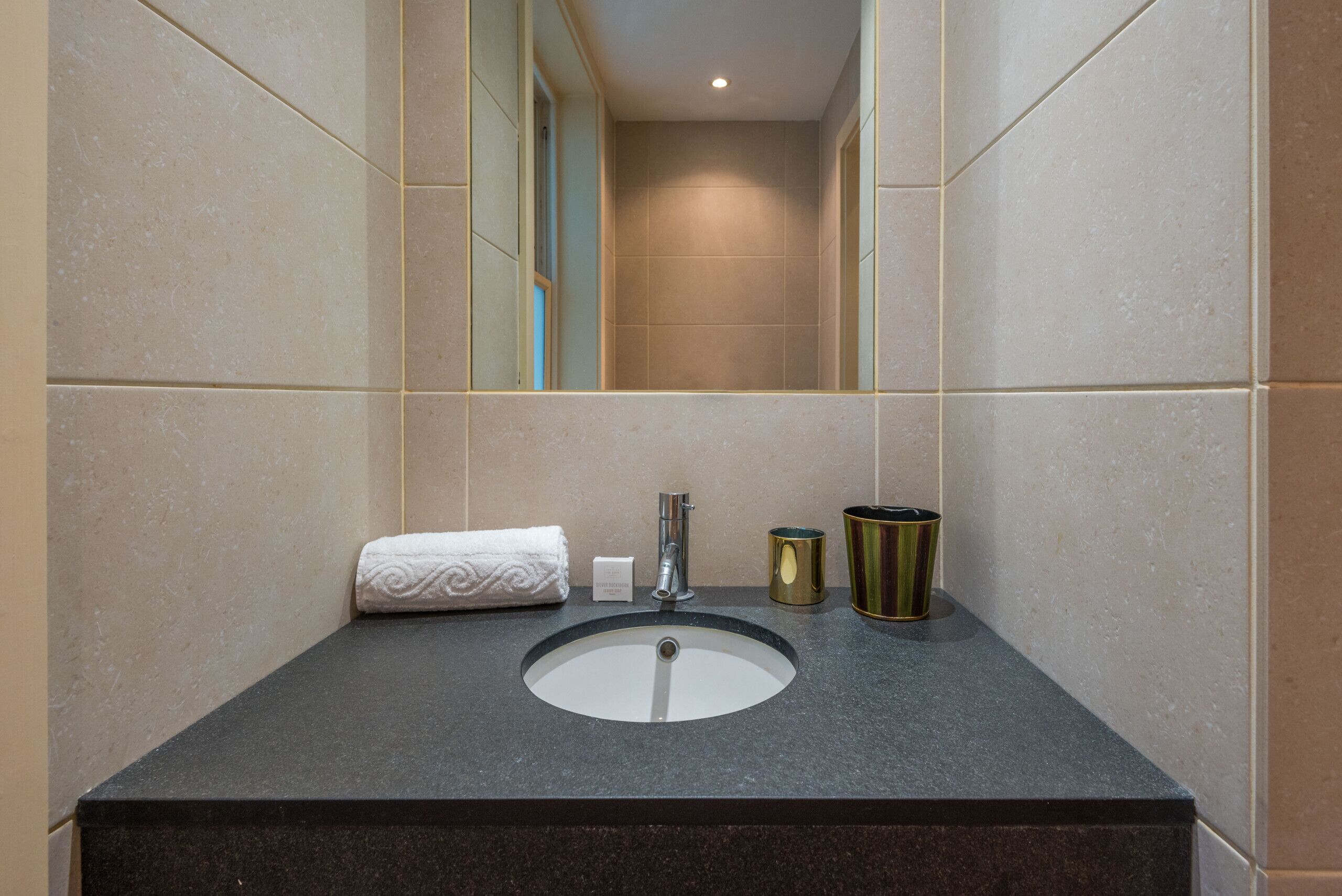 A bathroom with a sink, mirror, towel, and two containers.