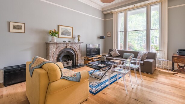 A living room with a fireplace, sofa, TV, and large windows.