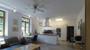 A modern kitchen with white cabinets, a central island, and built-in appliances. There is a dining area with a table and chairs, and a living room with a sofa and a coffee table. - Comfortable apartment on the Sturmhof (Grefrath)