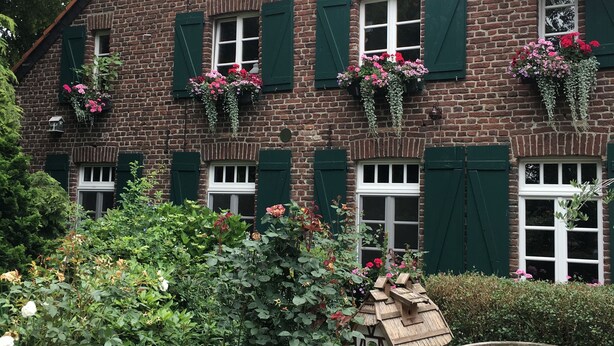 A brick building with green shutters and flower boxes. - Comfortable apartment on the Sturmhof (Grefrath)