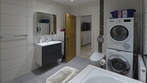 A modern bathroom with a sink, mirror, toilet, and stacked washer and dryer. - Comfortable apartment on the Sturmhof (Grefrath)