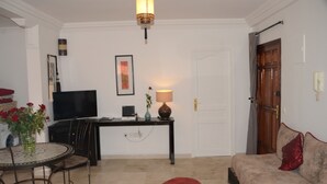 A living room with a sofa, a coffee table, a TV, a lamp, and a door. - CHARMING APARTMENT QUIET COMFORTABLE 2 PLACES C CENTER MARRAKECH GUELIZ (marrakech)