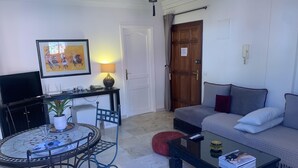 A living room with a sofa, a coffee table, a TV, a dining table with chairs, and a door. - CHARMING APARTMENT QUIET COMFORTABLE 2 PLACES C CENTER MARRAKECH GUELIZ (marrakech)