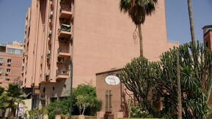 A multi-story building with balconies, a sign indicating a restaurant, and surrounding greenery. - CHARMING APARTMENT QUIET COMFORTABLE 2 PLACES C CENTER MARRAKECH GUELIZ (marrakech)