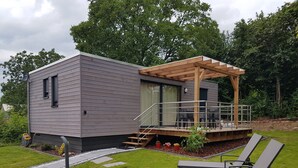 Une maison moderne dotée d’un patio couvert, d’un espace salon extérieur et d’un petit jardin.
